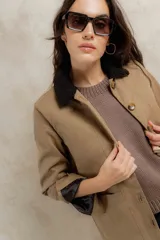 Campera color beige con cuello de corderito negro, cierre frontal con botones y forro interior. Presenta un diseño de corte recto y mangas largas con puños vueltos.