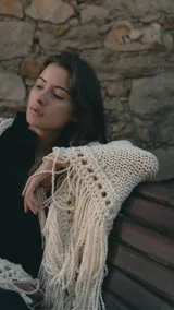 Ruana artesanal tejida en lana merino color crudo, con diseño de punto abierto en los bordes y flecos largos en todo el contorno.