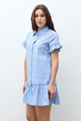 Vestido camisero corto color celeste con rayas blancas y finas rayas rojas. Presenta cuello camisero, botones frontales, mangas cortas con volados y un volado en el ruedo.