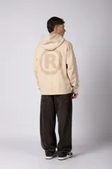 Buzo canguro color marrón con capucha, confeccionado en frisa de algodón. Presenta un diseño gráfico estampado en el frente con texto y logo circular, bolsillo tipo canguro y puños acanalados.
