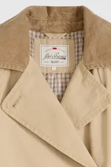 Trench coat largo de corte clásico en color beige, con diseño de doble botonadura, solapas amplias y cuello con detalle de textura. Presenta un estilo atemporal y estructurado.