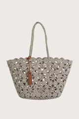 Bolso tipo shopper tejido en crochet con diseño de flores caladas. Presenta asas largas trenzadas y un detalle de etiqueta colgante en cuero sintético color suela.