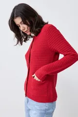 Chaqueta de punto color rojo, de corte entallado y manga larga. Presenta cuello redondo y cierre frontal con botones metálicos dorados texturizados.
