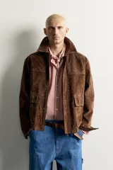 Parka de piel marrón tipo gamuza con cuello solapa, manga larga con puños de botones a presión y múltiples bolsillos de plastrón con solapa en el pecho y la cadera. Cierre frontal de cremallera oculta con solapa.