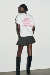 Camiseta blanca de manga corta y cuello redondo, con corte regular y bajo recto. Presenta el logo de "Sex & The City" estampado en color fucsia en el frente.