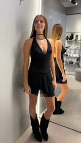 Vestido corto negro con escote halter y diseño drapeado en el torso. Presenta una falda con caída fluida y terminación en volado, con espalda descubierta.