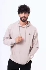 Buzo tipo canguro con capucha y cordones ajustables, confeccionado en felpa color beige. Presenta un pequeño logo bordado en el pecho y una etiqueta decorativa en el puño de la manga.