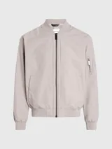 Campera tipo bomber de Calvin Klein en color beige, confeccionada en una mezcla de algodón y poliamida. Presenta cuello alzado, puños y bajo de punto canalé, cierre frontal de cremallera, bolsillos laterales de hendidura y un bolsillo adicional con cremallera en la manga izquierda con insignia de goma de la marca.