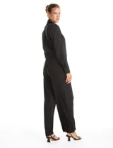 Enterito de crepe negro con cuello camisero, cierre frontal con botones y mangas largas. Presenta cintura elástica con cinto ajustable, bolsillos laterales funcionales y bolsillos simulados en el pecho.
