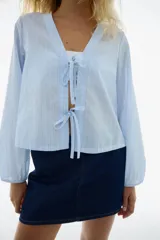 Blusa celeste a rayas blancas, de manga larga con elástico en los puños, escote en V y frente abierto con cierre de tiras para anudar.