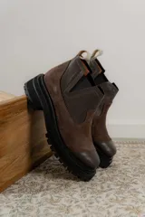 Bota tipo chelsea de punta redonda, confeccionada en una combinación de cuero texturizado y gamuza en tonos marrones. Presenta elásticos laterales negros y una suela track robusta de goma negra.