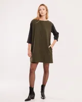 Vestido corto color verde militar con mangas 3/4 negras, cuello bote y bolsillos laterales.