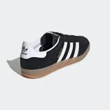 Championes Adidas Gazelle Indoor negros de gamuza con las tres tiras blancas y suela de goma color caramelo.