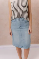 Pollera midi de denim celeste claro, de tiro medio y corte recto. Cuenta con bolsillos traseros, abertura central en la parte posterior y cierre frontal con botón y cremallera.