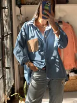 Camisa de corte oversize color celeste, confeccionada en una combinación de lino, lienzo y pana. Presenta cuello clásico, cierre frontal con botones y un bolsillo de parche en color beige en el pecho.