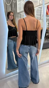 Top negro de tirantes finos, con escote en V y detalle de pedrería brillante en la parte delantera. Presenta diseño peplum con volados en la parte inferior.