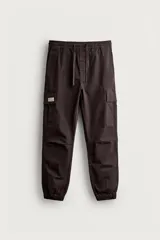 Pantalón cargo de corte slim fit en color marrón oscuro, confeccionado en tejido de algodón con elasticidad. Presenta cintura elástica con cordón ajustable, bolsillos laterales tipo cargo con solapa y bajo con puños elásticos.