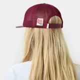 Gorra tipo trucker bordó, con frente de cuero sintético y paneles traseros de malla. Cuenta con visera plana y diseño con escudo bordado en la parte frontal.