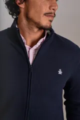 Cardigan de punto color azul marino, con cuello alto, cierre frontal completo y puños acanalados. Presenta el logo de la marca bordado en el pecho.