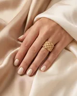 Anillo ancho de acero con baño de oro, con diseño de textura punteada en relieve.