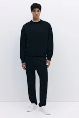 Buzo negro de tejido pesado con interior cepillado suave, cuello redondo y corte boxy. Presenta un diseño estampado en relieve tono sobre tono en el pecho.