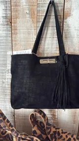 Cartera tipo tote bag de cuero negro con textura de reptil, cierre frontal metálico tipo torniquete y detalle de borla de flecos lateral. Cuenta con doble asa de hombro.