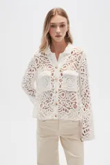 Camisa blanca de crochet con cuello camisero, cierre frontal con botones y dos bolsillos de parche en el pecho.