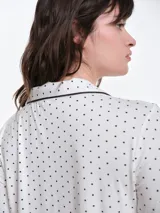 Camisa de pijama de manga larga con cuello solapa y cierre frontal de botones. Presenta un estampado sutil de pequeños corazones sobre una base de color gris melange, con detalles de ribete en contraste en el cuello y la botonera.