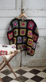 Sweater tejido a crochet con cuadrados de lana de colores sobre fondo negro, de corte holgado, cuello redondo y mangas largas.