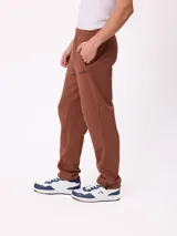 Pantalón tipo babucha de algodón y poliéster en color marrón, con cintura elástica, bolsillos laterales y logo de la marca bordado en la pierna izquierda.