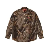 Camisa de manga larga con estampado de camuflaje tipo bosque, cuello abotonado y cierre frontal con botones. Cuenta con una pequeña etiqueta roja con el logo de la marca en el pecho.