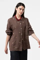 Camisa de lino color chocolate, de corte relajado y mangas largas con detalles bordados florales en contraste. Cuenta con cuello clásico y cierre frontal de botones.