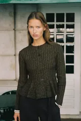 Chaqueta de punto canalé en color verde oliva jaspeado, con cuello redondo, manga larga y cierre frontal con botones. Presenta un diseño entallado con bajo en evasé tipo peplum.