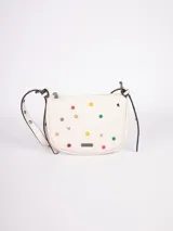 Cartera bandolera color crema de símil cuero, con apliques frontales de tachas redondas de colores y estrellas plateadas. Tiene correa regulable con hebillas y cierre superior con cremallera.