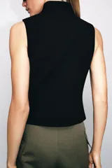 Chaleco negro de cuello subido y manga sisa, con cierre frontal oculto y detalle de botones decorativos metálicos en estilo militar.