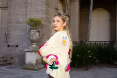 Sweater holgado de lana merino color marfil, con mangas con diseño de ochos y apliques bordados de flores en 3D de diversos colores.