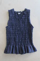 Top de lino a rayas azules y blancas, sin mangas, con diseño fruncido tipo nido de abeja en el torso y doble volante en el bajo.