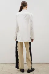 Pantalón de corte recto y tiro alto, confeccionado en algodón con diseño bicolor que combina paneles laterales en negro y panel central en beige, unidos por costuras visibles a contratono.