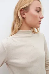 Blusa beige claro con cuello alto y mangas largas, con pequeños brillos.