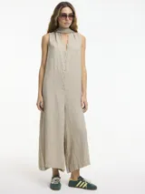 Mono largo de lino en color beige, con escote en V y cierre frontal mediante botones. Presenta un diseño sin mangas, de calce amplio con piernas anchas y bolsillos laterales ocultos. Incluye un lazo regulable para ajustar a la cintura.