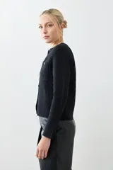 Chaqueta tejida negra con cuello redondo, cierre frontal con botones dorados, bolsillos delanteros y corte clásico.