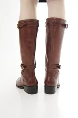 Bota de caña alta de cuero liso negro, con diseño clásico, detalles de hebillas metálicas, cierre lateral y taco bajo.