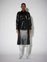 Camisa negra de manga larga con efecto cuero y acabado brillante. Presenta cuello clásico, cierre frontal de botones y puños abotonados. El diseño incluye un ligero volumen en las mangas.