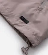Campera rompevientos de color gris oscuro, con capucha ajustable mediante cordones, cierre frontal por cremallera y bolsillos laterales con cierre. Presenta puños elásticos y un diseño liso y minimalista.