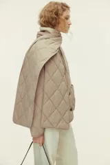 Campera acolchada de color beige con diseño guateado en rombos, hombros caídos, cuello redondo, cierre frontal de botones y bolsillos parche delanteros. Incluye una bufanda a juego que se abrocha en la nuca y cuenta con aislamiento térmico THERMOLITE.