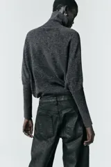 Jersey de punto liso color gris oscuro, con cuello subido y diseño de manga murciélago con sisa amplia que se ajusta hacia la muñeca.
