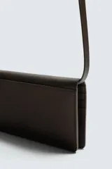 Cartera tipo bandolera de piel color marrón oscuro, con solapa y cierre a presión. Incluye seis ranuras para tarjetas, una ranura para billetes y un monedero interior con cierre de cremallera. Posee un asa de hombro ajustable y extraíble.