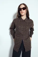 Camisa tipo leñadora de corte oversize, con estampado de cuadros en tonos negro y marrón. Presenta cuello clásico, cierre frontal con botones y mangas largas con puños abotonados.