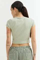 Remera crop top de manga corta, color verde claro, con textura acanalada y texto en relieve en el pecho.