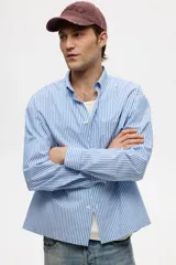 Camisa de corte relajado confeccionada en tejido de algodón con estampado de rayas verticales. Presenta cuello americano, cierre frontal con botones, un bolsillo en el pecho y mangas largas con puños abotonados.